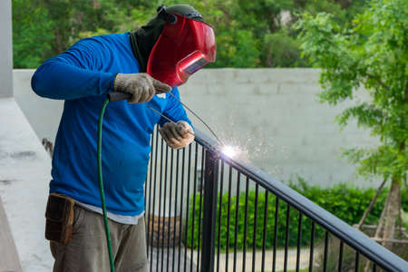 Closeup hands of welder welding the steelwork of black fence with sparking light and smokeの写真素材