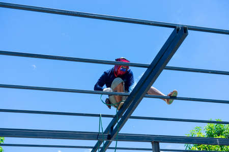 Worker welding the steel structure of roof with arc welding machine and blue sky in backgroundの写真素材