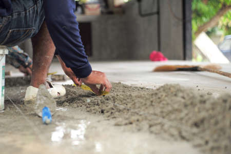 Selective focus on leg and hands of worker mearsuring the floor during installation the floor tiles in the ouse under constructionの写真素材