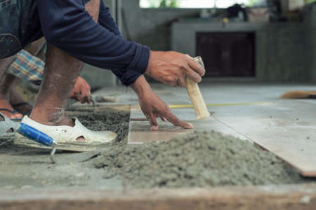 Motion blurred hand of worker installing the floor tile by wooden hammer at the construction site