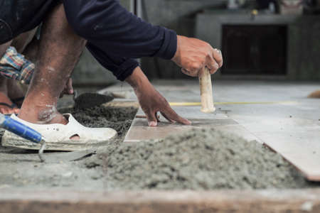 Motion blurred hand of worker installing the floor tile by wooden hammer at the construction siteの写真素材