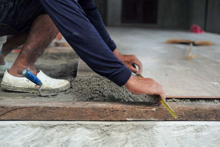 Selective focus on leg and hands of worker measuring the floor during installation the floor tiles in the ouse under constructionの写真素材