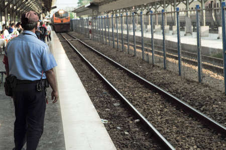 Rear view of security guard in the uniform works at the platform of train station while the train is...