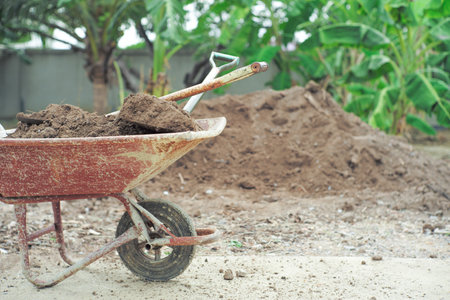 Closeup steel cart carrying the soil with shovels with blurred pile of soil and landscape in backgroundの写真素材