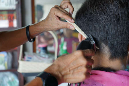 Closeup hands of hairsltylist and rear view of man having a hair cut by electrical battalion.の写真素材