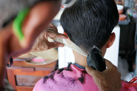 Closeup hands of hairsltylist and rear view of man having a hair cut by electrical battalion.の写真素材