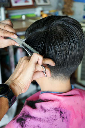 Closeup hands of hairsltylist and rear view of man having a hair cut by scissors and comb.の写真素材