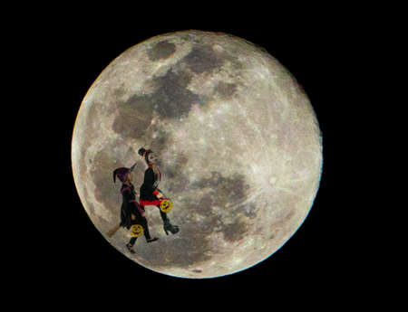 Two girl in witch clothes ride the broom in the air with super moon in backgroundの写真素材