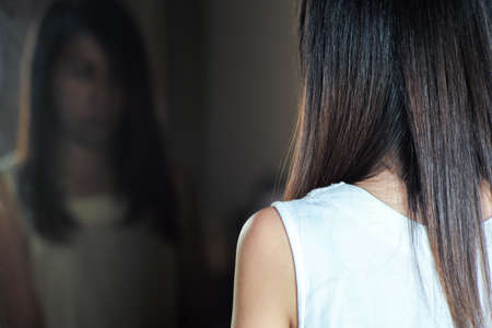 Closeup shoulder of woman looks at her reflection in the mirror