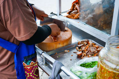 Delicious stewed ear pork at the street food. Motion blurred hand of seller chops the pork on cutting board.の写真素材