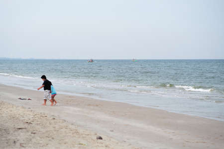 Seascape with fishing boat floating in the sea with blurred foreground of little boy and girl playing on the beachの写真素材