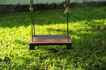 Closeup old wooden swing hanging from the tree in the backyard gardenの写真素材