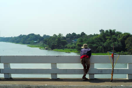 Rear view of man looks for the fish in  the river for fishing by the wooden gun with landscape in backgroundの写真素材