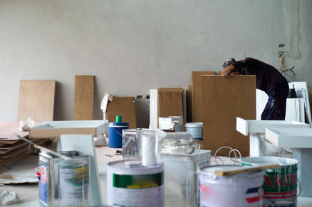 Worker making the wooden board for interior furnitures in the house under construction with blurred foreground of color tanksの写真素材