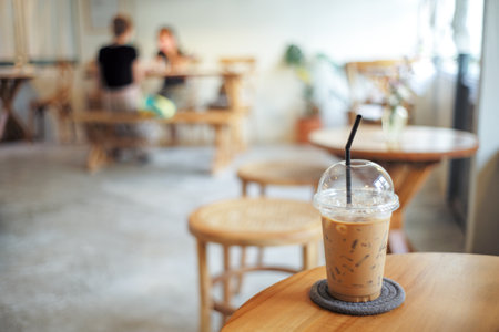 Closeup plastic glass of ice coffee on the wooden table with blurred customers in background. Co working space conceptの写真素材
