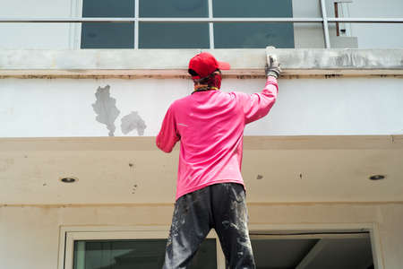 Rear view of worker removing the old color out of the surface of the cement wallの写真素材