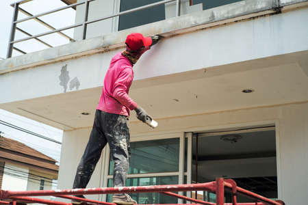 Rear view of worker removing the old color out of the surface of the cement wallの写真素材