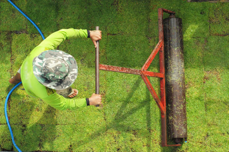 Top view worker pushes the heavy steel drum on the grass field during growing processの写真素材