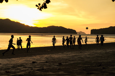 Silhouette group of people playing the football on the beach in the sunset with seascape and...
