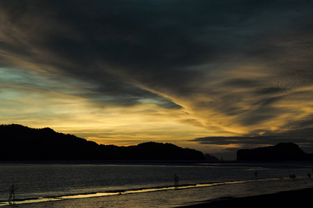 Cloudy sky of sunset with silhouette of mountain in background and beach in foreground. Twilight sky with seascape.の写真素材