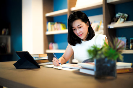 Portrait beautiful Asian woman works at the home office with blurred shelf of books in background