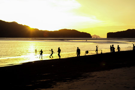 Silhouette group of people playing the football on the beach in the sunset with seascape and mountain in backgroundの写真素材