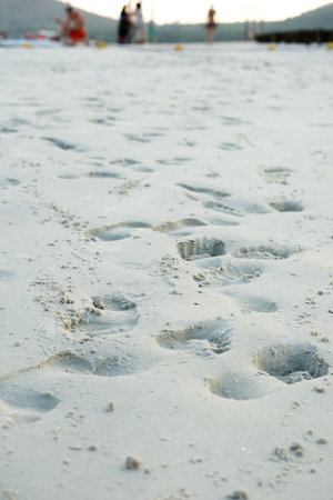 Closeup footprints in the sand with blurred group of people in backgroundの写真素材