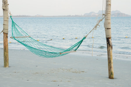 Empty swing weaved by rope hanging on the wooden poles on the beach with seascape backgroundの写真素材