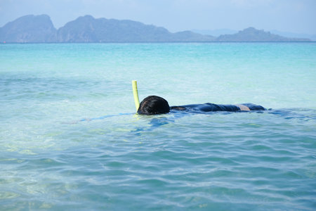 A girl is floating on the surface of the sea and sees the reef and fish under the water by snorkel maskの写真素材