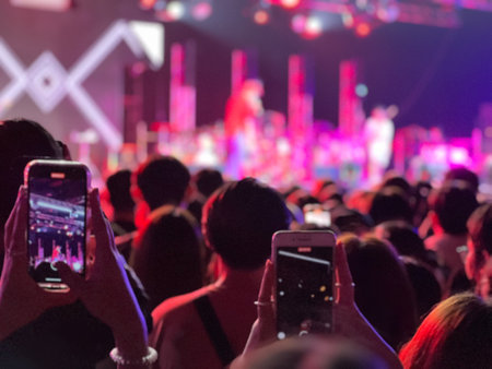 Rear view crowded of people enjoy and records the singer on the stage by mobile phone with blurred light and sound of stage in backgroundの写真素材