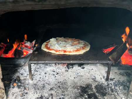 Selective focus on the pizza baking in the traditional oven by the flame of charcoalの写真素材