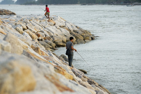 The people fishing at the coast of the sea by the fishing rod with seascape in backgroundの写真素材