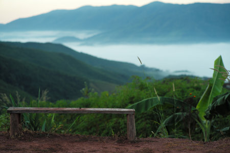 The empty wooden bench on the mountain with the view of mountain layers and fluffy white fog in backgroundの写真素材