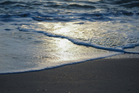 Closeup wave surfing on the sand beach with reflection of the sun light on the surface of the waterの写真素材