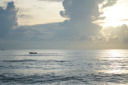 Silhouette of fisherman driving the long-tail boat in the calm sea with sunrise in backgroundの写真素材