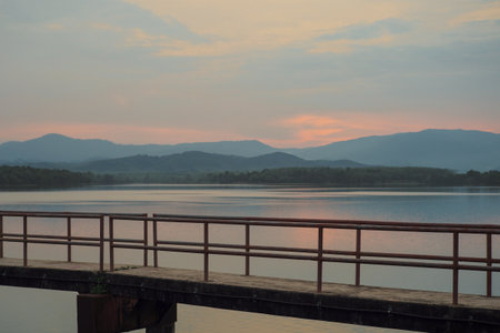 The concrete walkway into the water reservoir with the horizontal line of the mountains during the sunsetの写真素材