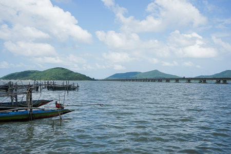 Long tail boat floating on the shore with long concrete bridge and mountain in backgroundの写真素材