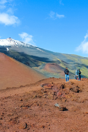 Mount Etna, Sicily, Italy - April 9th 2019: Couple of tourists standing on the Silvestri craters overlooking the very top of Etna volcano. Snow on the very top of the mountain. Popular destination.のeditorial素材