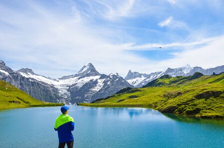 Young man operating the flying drone over beautiful Bachalpsee in the Swiss Alps. Drone cameras are used for aerial photography and footage. Switzerland landscape. Drone noise.の写真素材
