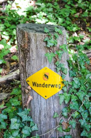 Yellow hiking trail mark on a wooden stump in the forest. Sign TRANSLATION: Wanderweg - trail, hiking path in German. Tourist signs help for orientation on hiking paths. Trailblazing, waymarking.の写真素材