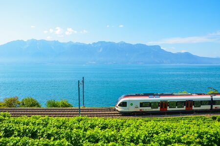 St. Saphorin, Switzerland - July 26, 2019: Train on scenic railway leading on the coast of Lake Geneva in Switzerland. Green vineyard on adjacent slope. Lavaux wine region. Mountains in background.のeditorial素材