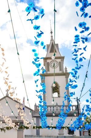Colorful street decoration hanging on the street in front of the Roman Catholic church in Loreto, Madeira, Portugal. Portuguese religious festival decor. Paper flowers in blue and white color.の写真素材
