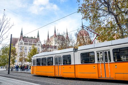 Budapest, Hungary - Nov 6, 2019: Public yellow tram riding in front of the Hungarian Parliament...