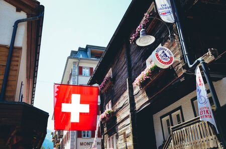 Zermatt, Switzerland - July 10, 2019: National flag of Switzerland waving on the street in the popular Alpine resort. Swiss flag. White cross in the center of a square red field. Swiss concept.のeditorial素材