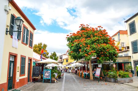 Funchal, Madeira, Portugal - Sep 10, 2019: Street in Madeiran capital with typical restaurants and cafes. People drinking and eating on outdoor terraces. Colonial architecture. Historical old town.のeditorial素材