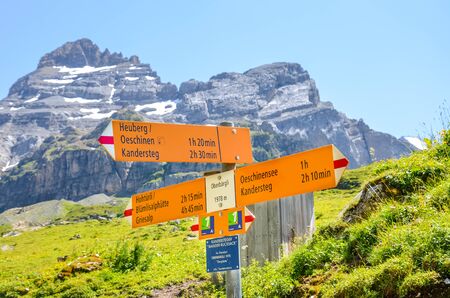 Kandersteg, Switzerland - August 4 2019: Tourist sign in Oberbargli on the trail to Oeschinensee lake in the Swiss Alps. Information sign giving directions and walking time. Summer Alpine landscape.のeditorial素材