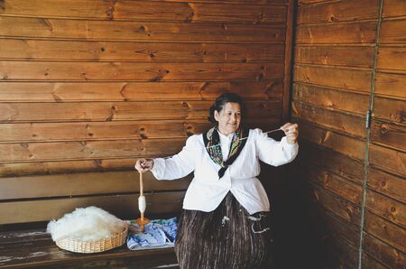 Santana, Madeira, Portugal - Sep 24, 2019: Woman in traditional costume sitting on a wooden bench and hand spinning wool. Old craftsmanship, handcraft. Taken in Madeira Theme Park.のeditorial素材