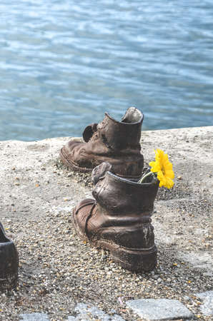 Budapest, Hungary - Nov 6, 2019: Shoes on the Danube Bank. Monument to honour the Jews who were killed by fascists during World War II. Iron shoes with yellow flower. Blurred Danube in the background.のeditorial素材