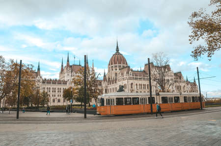 Budapest, Hungary - Nov 6, 2019: Public yellow tram riding in front of the Hungarian Parliament...