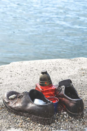 Budapest, Hungary - Nov 6, 2019: Shoes on the Danube Bank. Monument to honour the Jews who were killed by fascists during World War II. Iron shoes, red candle. Blurred Danube in the background.のeditorial素材